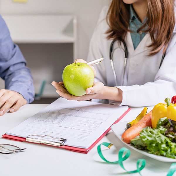 Nutritionist holding an apple out to a patient with a plate of vegetables in the foreground
